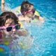two children swimming in a pool with floaties and goggles on a sunny summer day