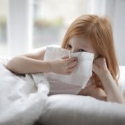 child blowing nose into tissue while laying in bed