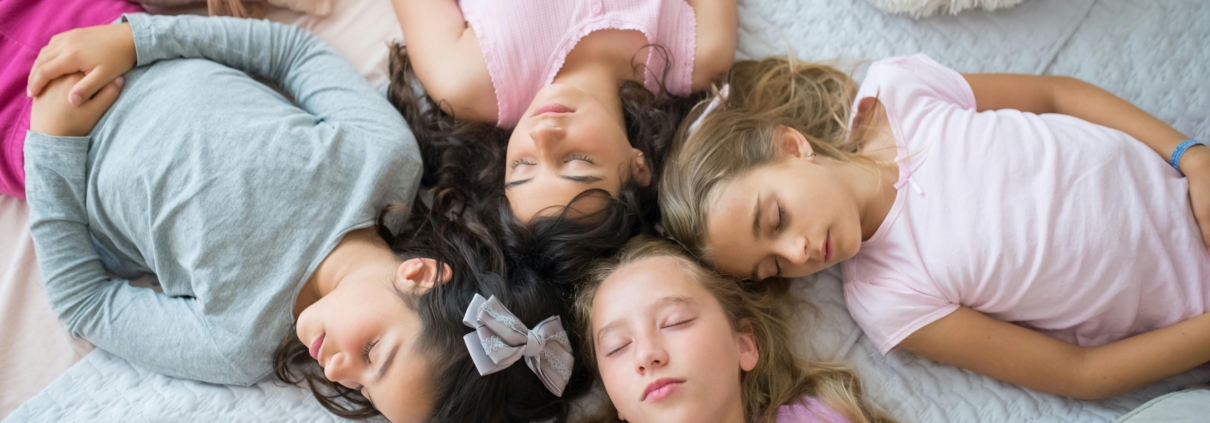 young girls at a sleepover with their heads touching as they lay in bed